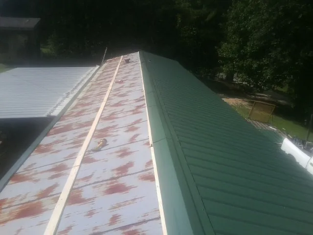Old rusted panels beside newly installed green metal roofing — Wind Damage Roof Repair by Roofing Brothers in Agency