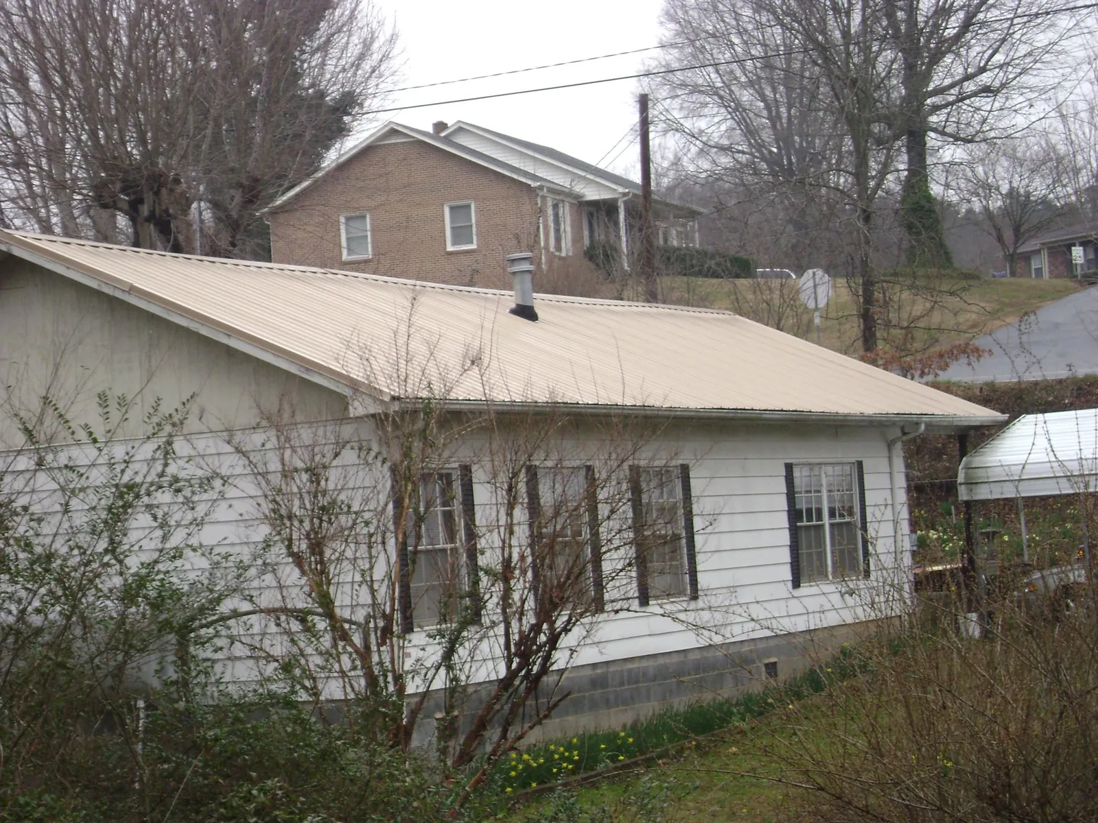 Tan metal roof on a white sided house set into a hillside — Commercial Roofing by Roofing Brothers in Agency